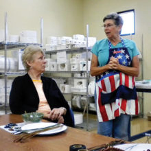 Jackie Graham explains how to pine-needle weave on pottery bowls to Sandy Holt in a recent class.